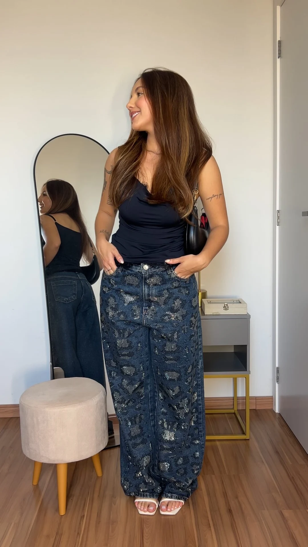 Clara Sol de regata escura e jeans, mostrando seu look em frente ao espelho